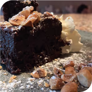 Un dessert gourmand : un brownie au chocolat avec des noix caramélisées, de la crème fouettée et du sucre glace.